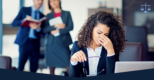 A woman sitting at her desk upset about something as two employees stare at her in the distance.