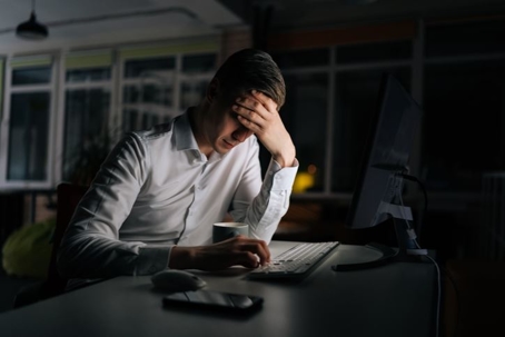 man working late on computer with head in hand