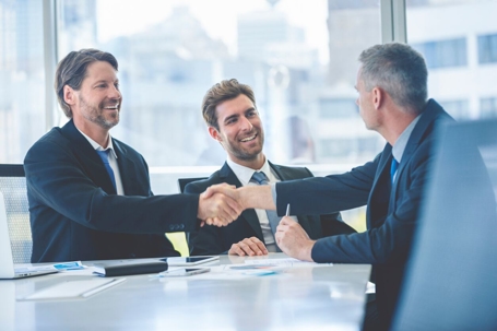 Businessmen shaking hands at the board room table.